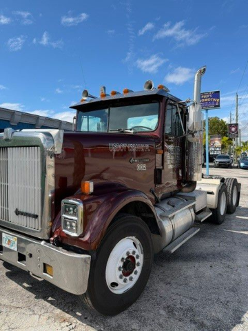 Maroon semi-truck parked on a sunny street under a blue sky