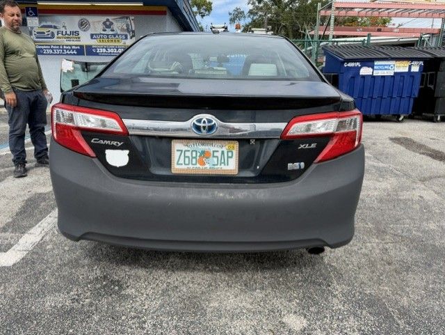 Rear view of a black Toyota Camry with a Florida license plate parked in a lot, man standing nearby.