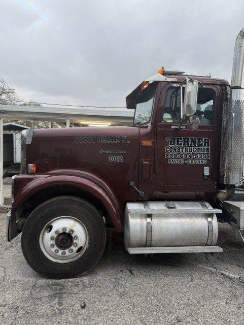 Maroon Werner truck parked on a gravel lot under a cloudy sky