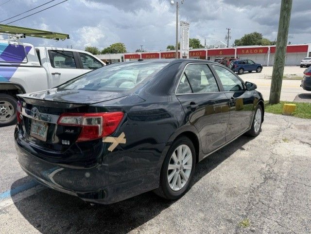 Black sedan parked in a lot, viewed from the rear-left side under cloudy skies.