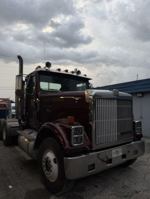 Maroon semi truck with chrome grille parked outdoors under cloudy skies