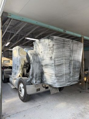 Truck carrying a large, shrink-wrapped load parked under a covered structure