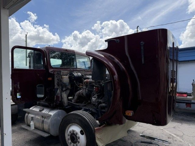 Semi-truck with hood open, exposing the engine, parked outdoors under a cloudy sky.