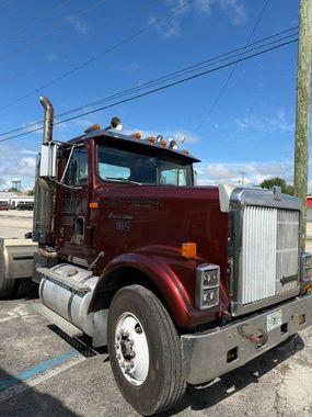 Maroon semi truck parked outdoors under a clear blue sky