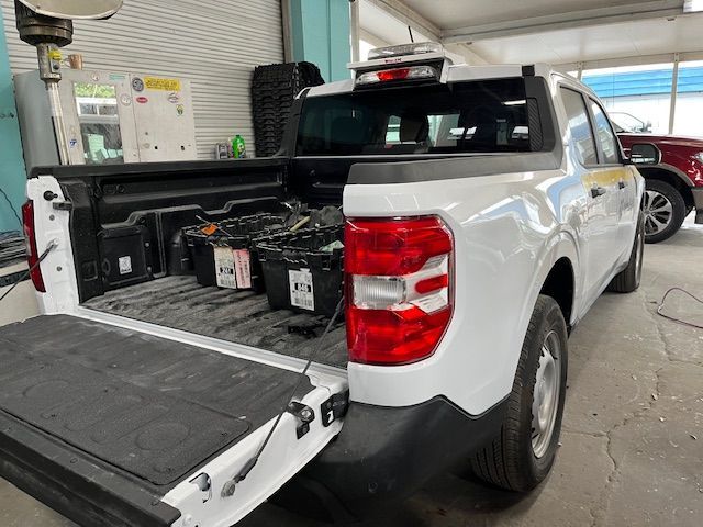 White pickup truck with tailgate open, exposing several batteries in the truck bed inside a garage