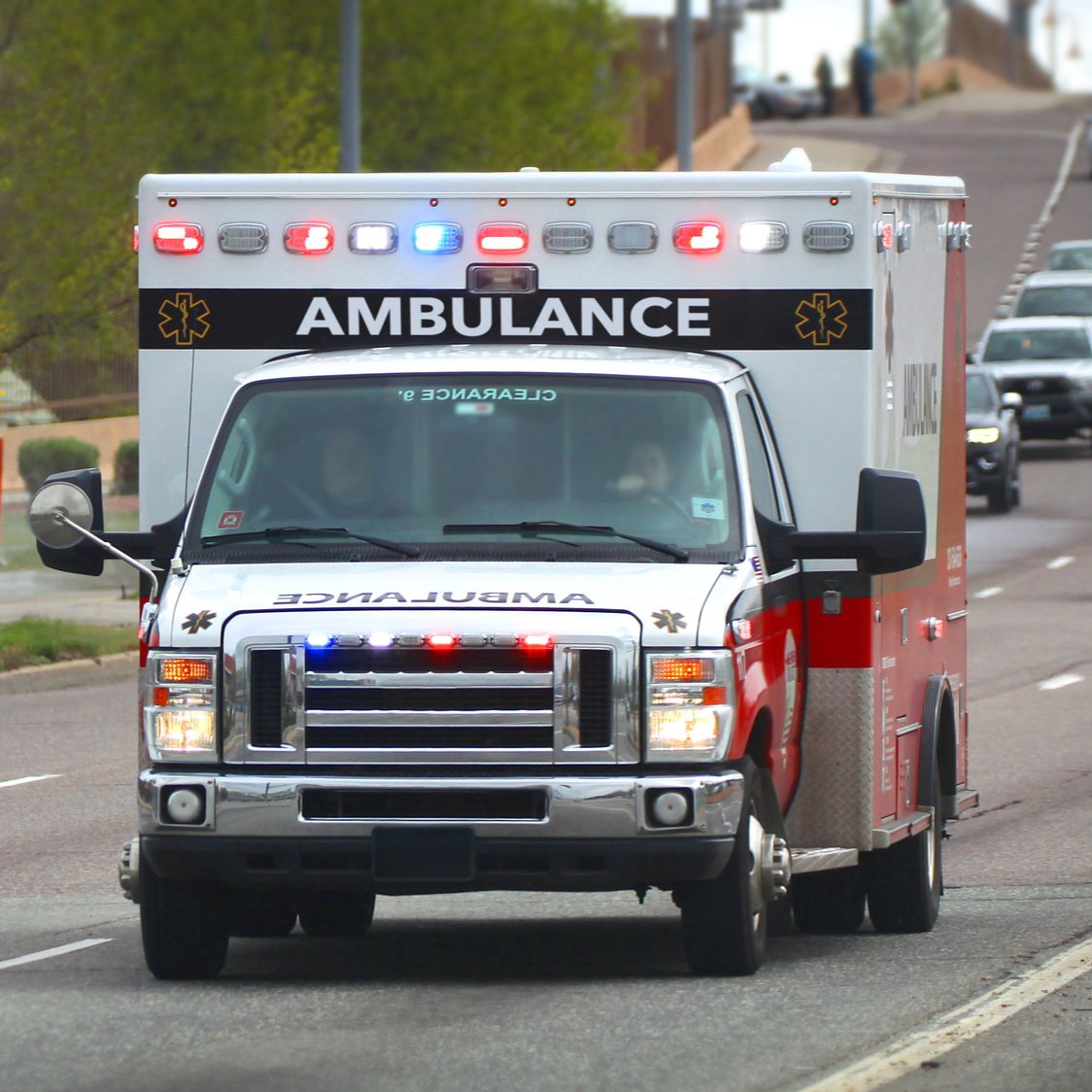 White and red ambulance driving on a city street with emergency lights flashing