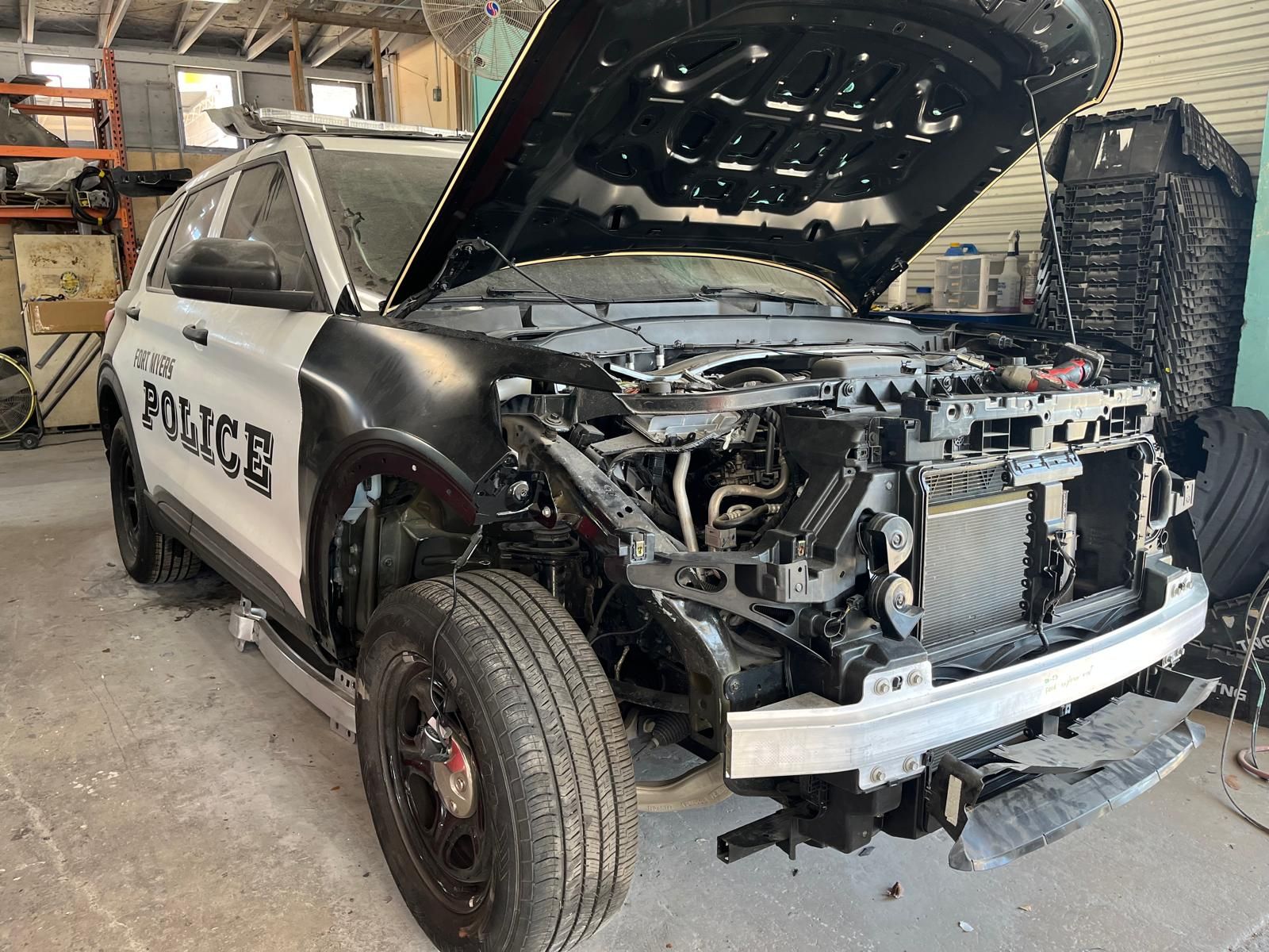 Damaged black-and-white police SUV with front end torn open inside a workshop