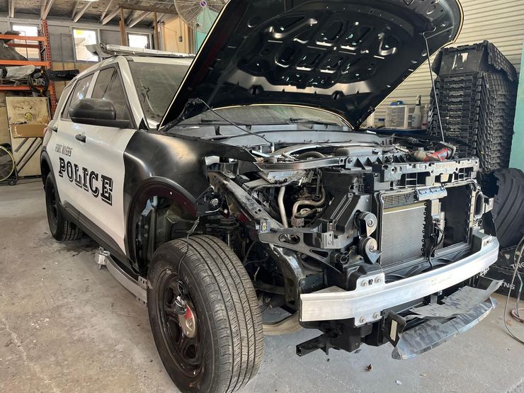 Damaged black-and-white police SUV with front end torn off inside a garage