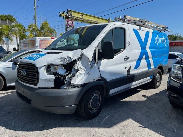 Damaged white Ford van with blue Xfinity logo and front-left collision damage in a parking lot