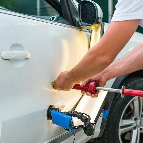 Person using dent removal tools on a white car door, in an outdoor setting.