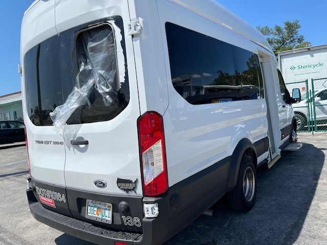 White Ford Transit van parked outdoors at a dealership, rear-left view with cracked rear window covering.