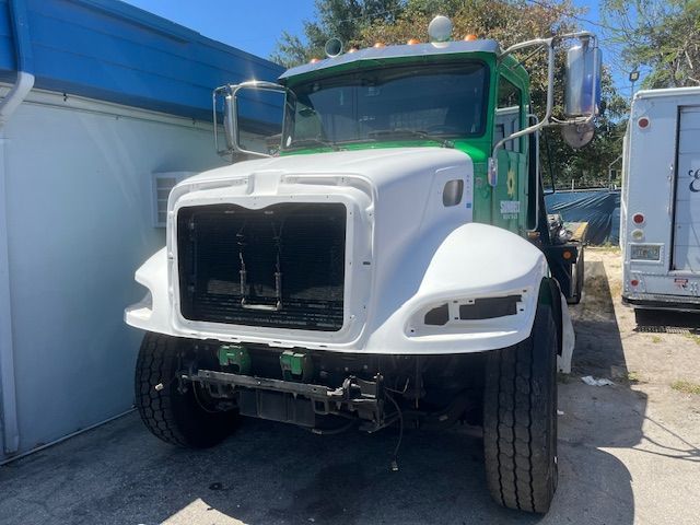 White semi-truck cab with green roof parked outdoors between buildings
