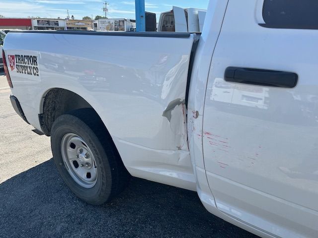 White pickup truck with side damage and a dented rear door panel in a parking lot