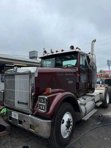 Maroon semi-truck parked in an industrial lot under cloudy skies.