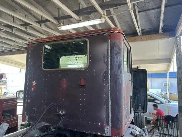 Black truck cab in a garage, viewed from the rear with a person working nearby.