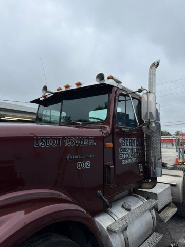 Maroon tow truck with chrome exhaust pipes parked on a roadside under cloudy sky
