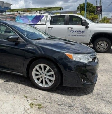 Dark sedan parked beside a white Quantum pickup truck outdoors on a cloudy day