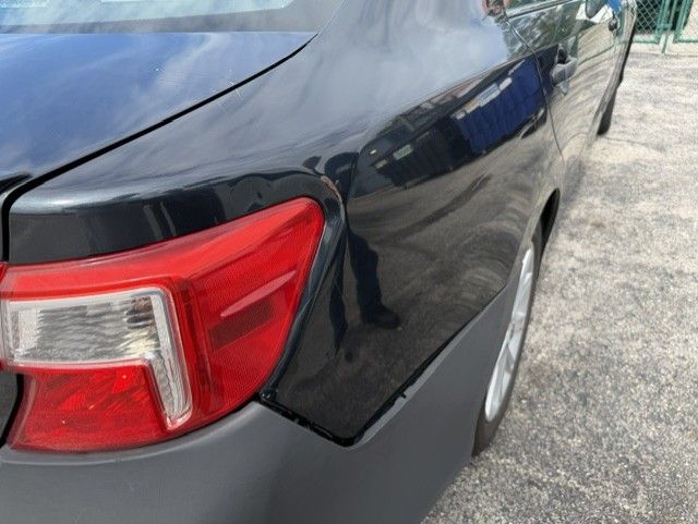 Close-up of a black car’s rear taillight and dented side panel in a parking lot.