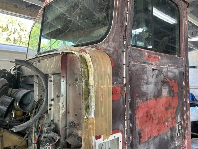 Old truck cab undergoing repair, with rusted red and gray body panels exposed.