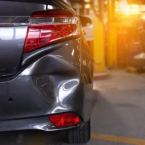 Damaged gray car bumper in a repair shop, with dent and broken taillight.