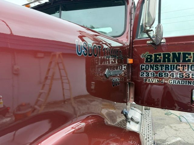 Red semi-truck cab with visible door signage for Bernal Construction at a work site