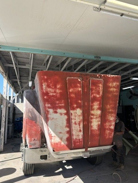 Red dump truck with weathered red bed parked under a roofed garage.