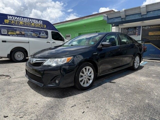 Black sedan parked in a lot beside a white van and green building under a cloudy sky