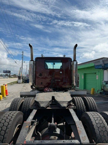 Semi-truck cab on a road beside a green trailer under a cloudy blue sky