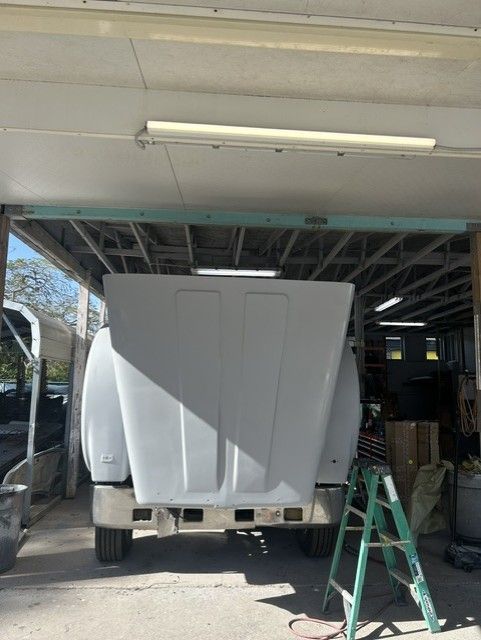White boat hull on a trailer inside a garage, with a green ladder nearby.