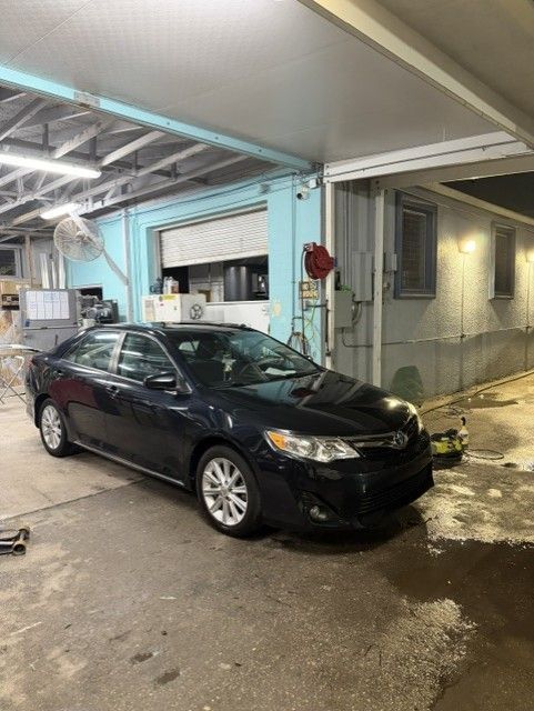 Black sedan parked under a covered garage beside a light blue building at night