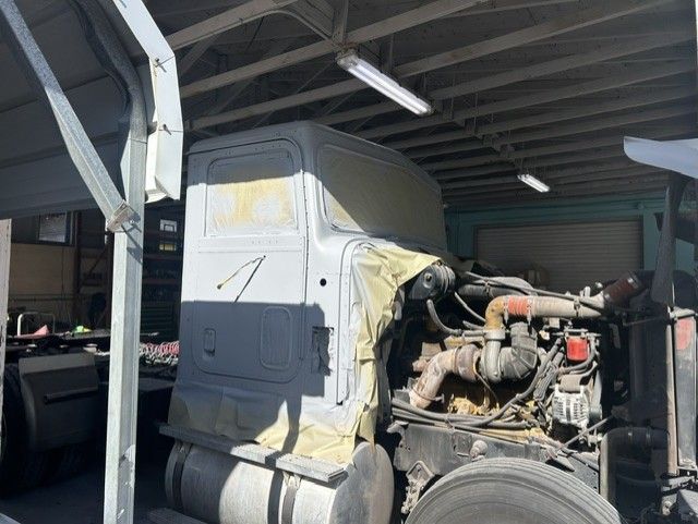 Truck cab being repaired in a workshop, with engine exposed under a roofed bay.