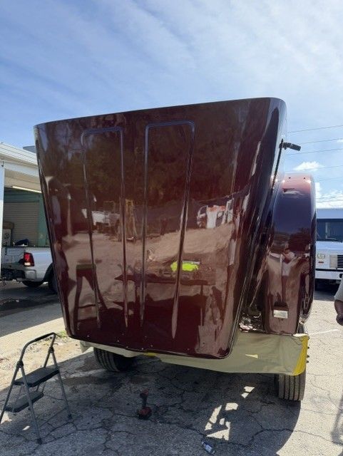 Brown RV front parked in a driveway, with a yellow step stool beneath it and a second RV beside it.