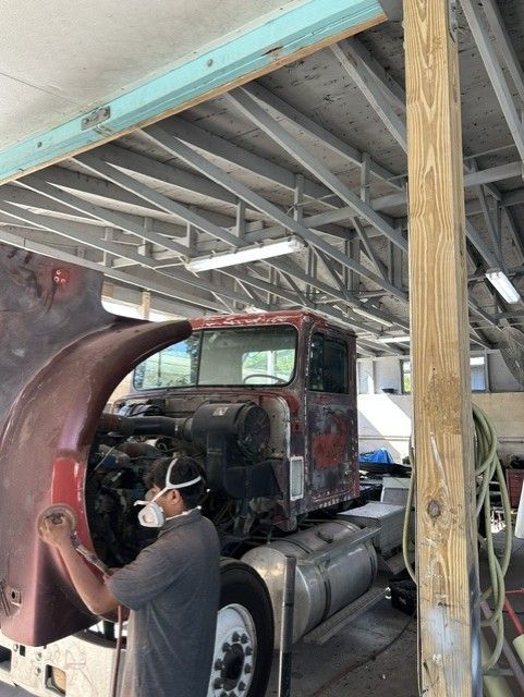 Man working on a red semi truck inside a garage with exposed beams and hanging wires
