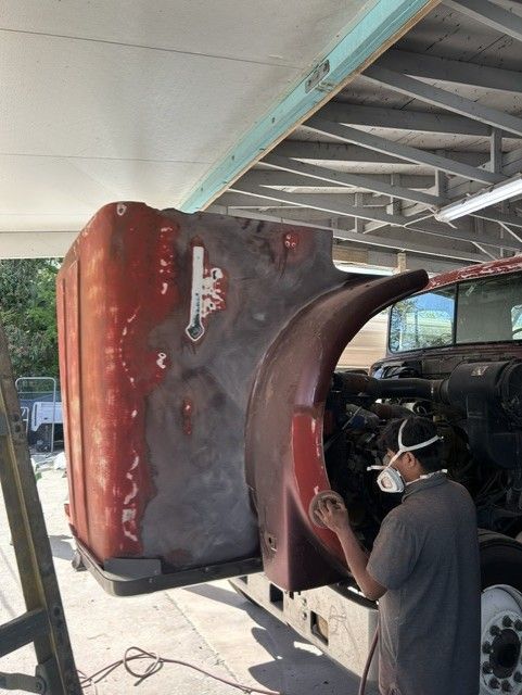 Person spray-paints a large red and black vehicle body in a garage.