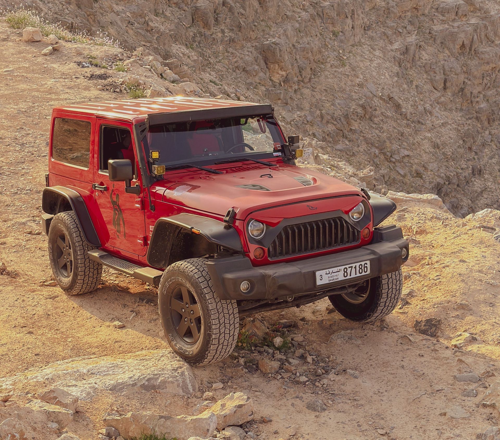 Red off-road Jeep Wrangler on a rocky dirt trail in a barren landscape