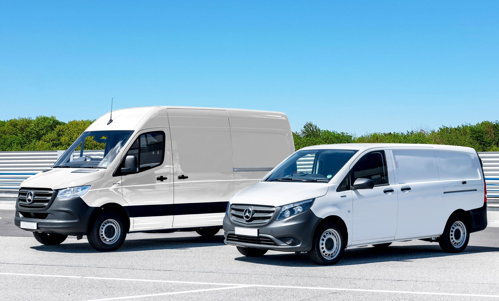 Two white delivery vans parked side by side on a sunny lot under a clear blue sky