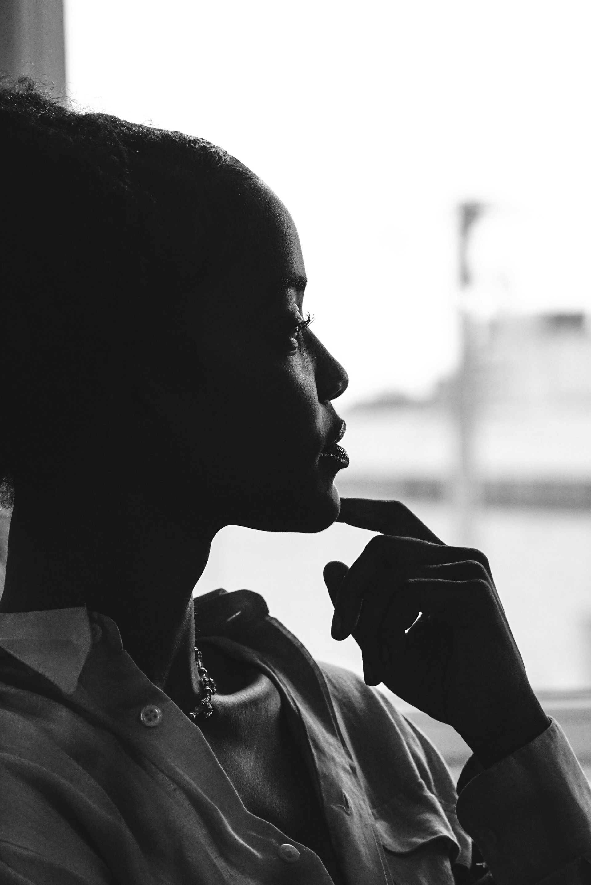 Silhouette of a person in profile by a bright window, resting their hand on their chin.