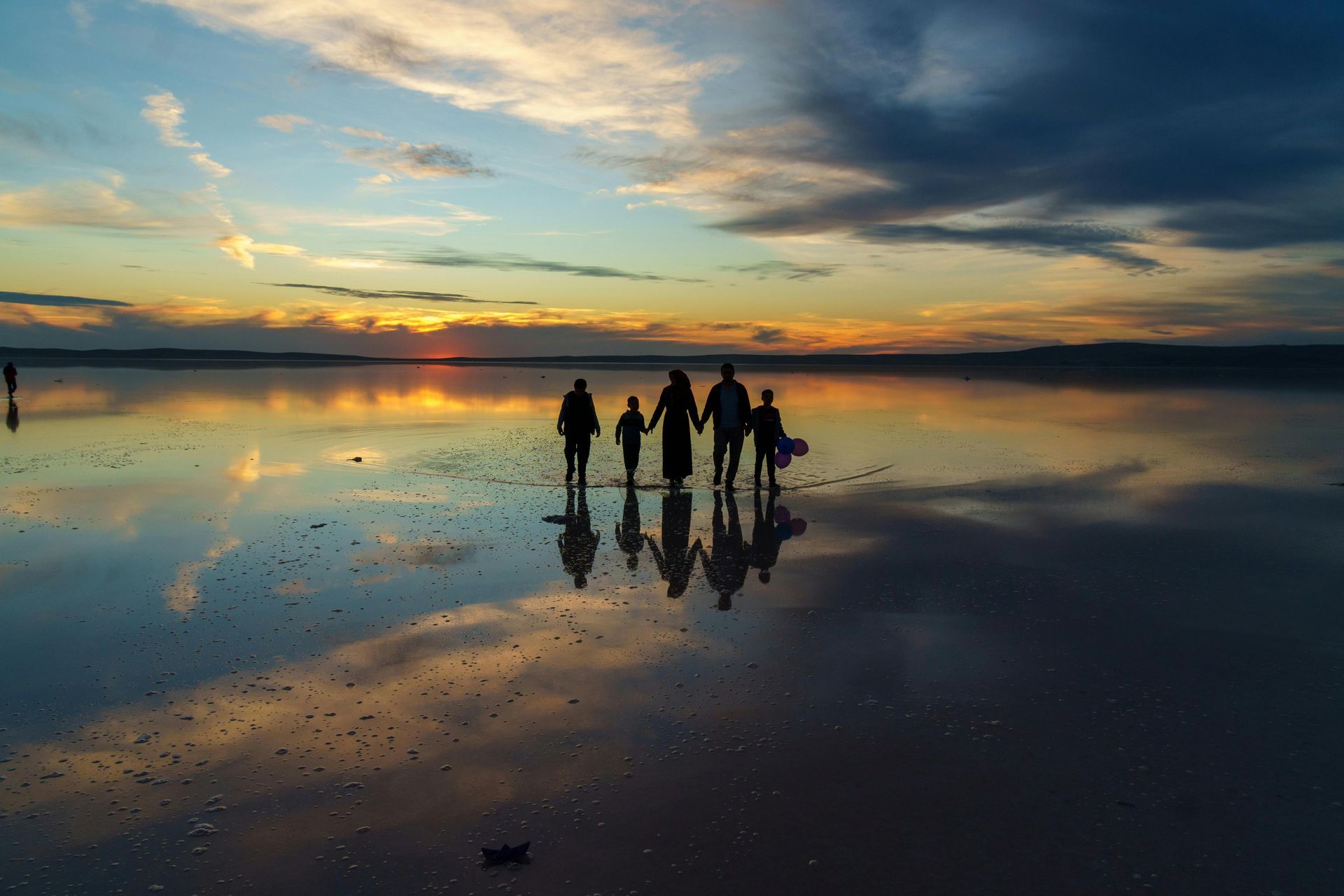 People silhouetted on a reflective beach at sunset under dramatic clouds