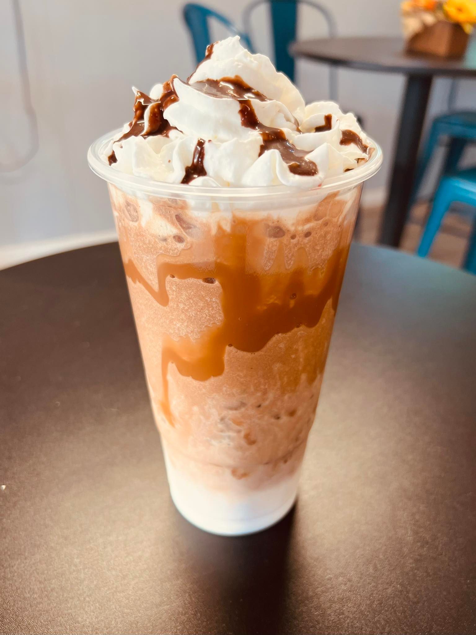A tall plastic cup of iced blended coffee topped with whipped cream and drizzled with caramel and chocolate sauce.