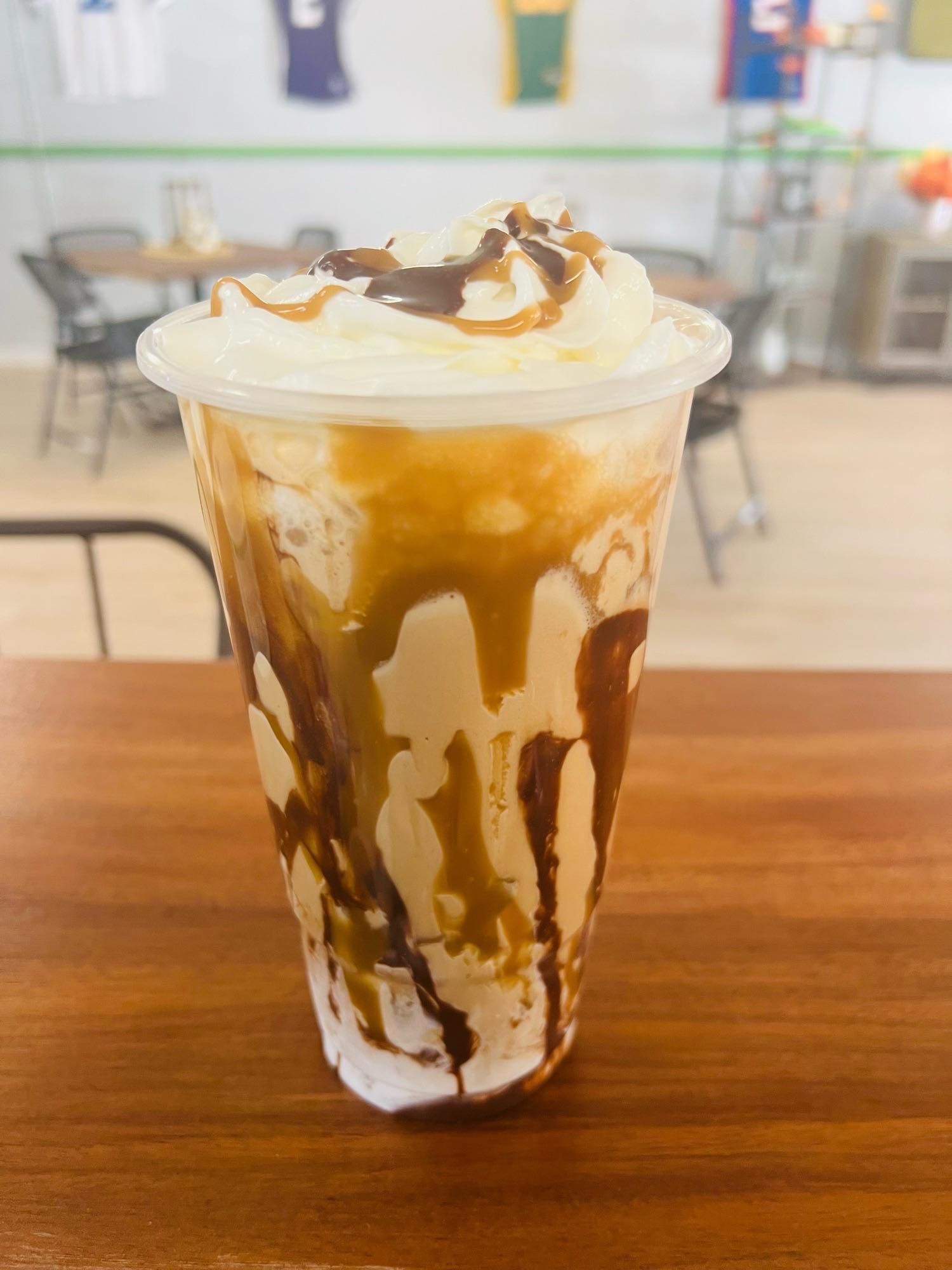 A plastic cup of iced coffee topped with whipped cream, drizzled with thick ribbons of chocolate and caramel syrup.