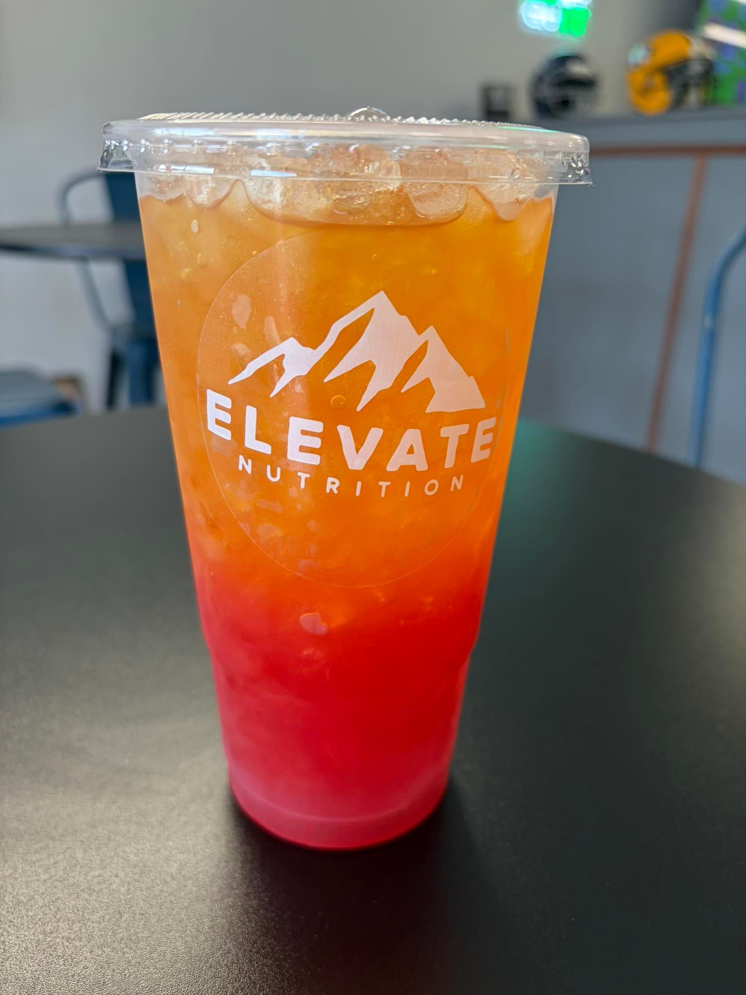 An iced tea with a vibrant red and orange gradient, in a clear plastic cup branded with the Elevate Nutrition logo.