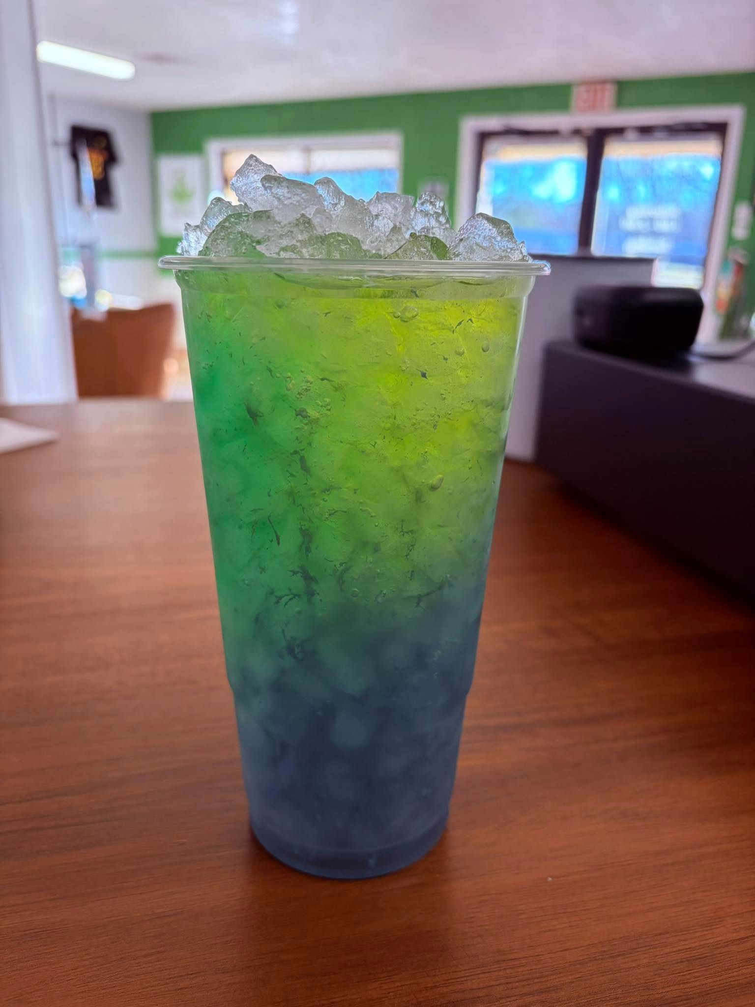 A plastic cup filled with ice and a layered drink transitioning from deep blue at the bottom to lime green at the top.