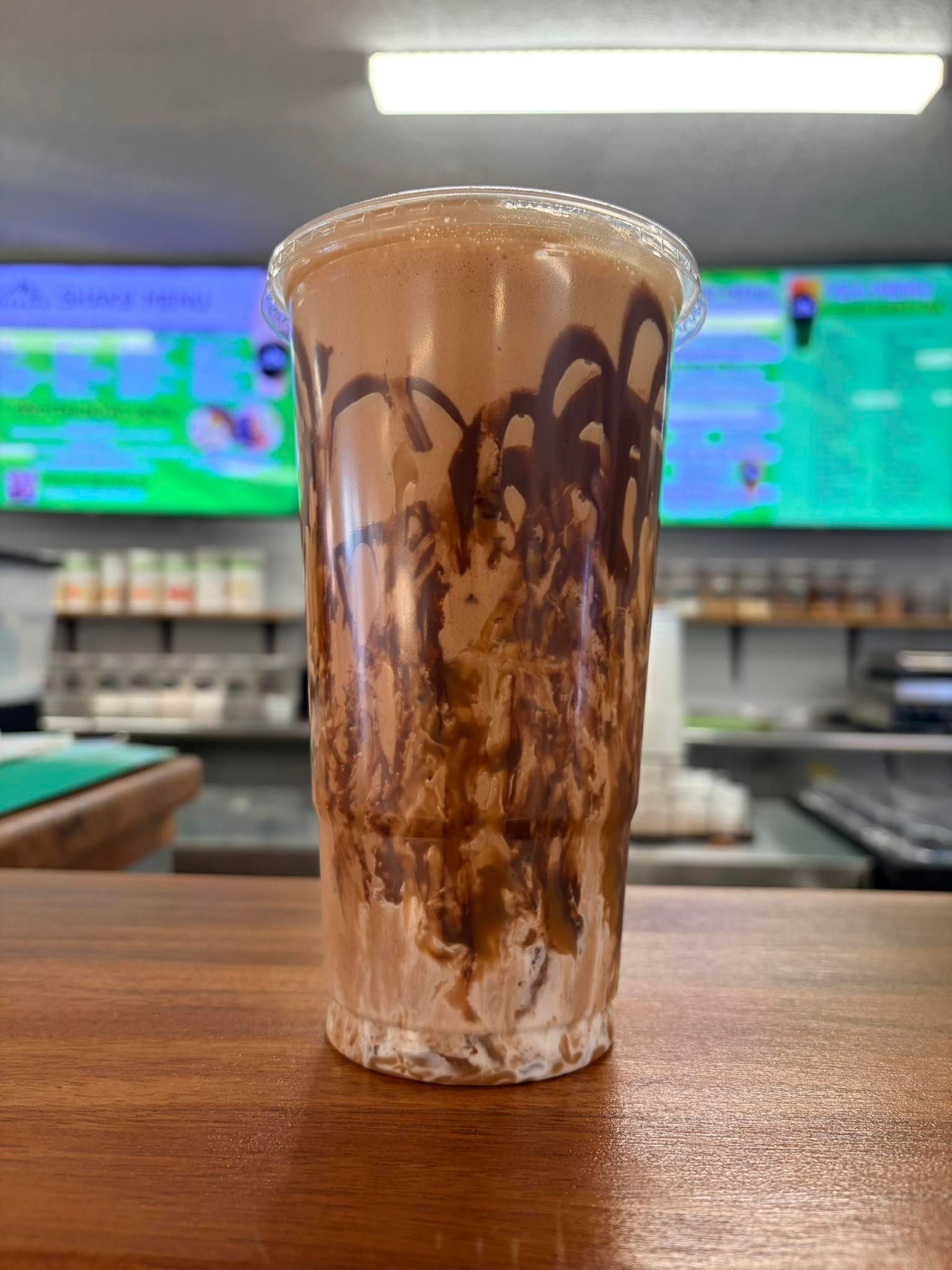 A large, blended coffee drink in a clear plastic cup, drizzled with chocolate syrup on the inside, sitting on a counter.
