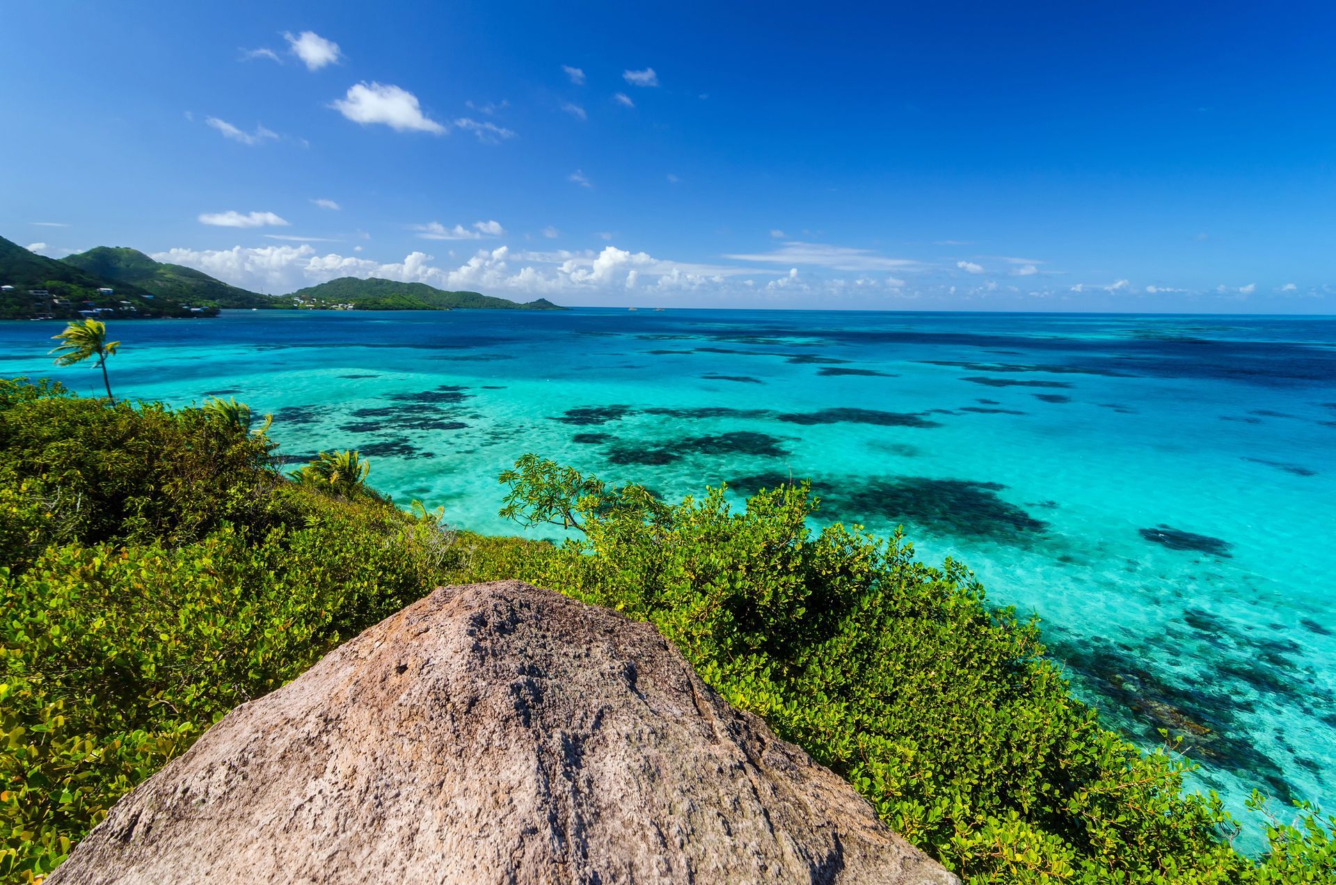 Una vista de una isla tropical con una roca en primer plano y el océano en el fondo.