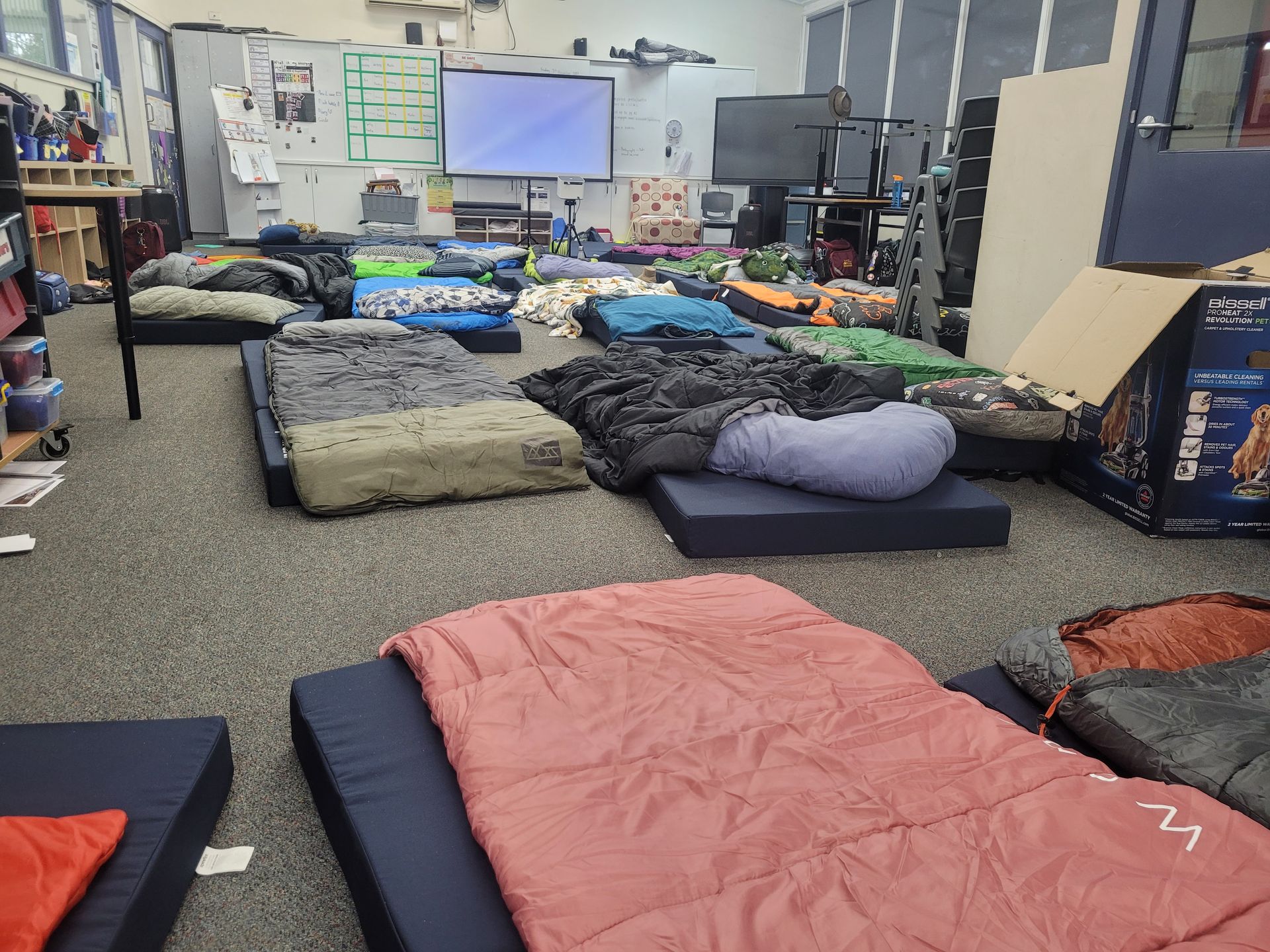 Indoor space with mattresses and sleeping bags set up on the floor.