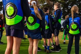 Children wearing blue vests with green and blue targets, standing on a green field.