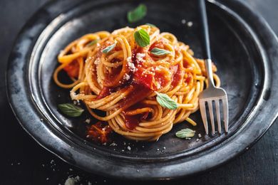 Plate of spaghetti with tomato sauce and basil on a dark dish, with a fork beside it