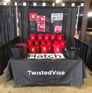 TwistedVise booth display with red branded buckets, black bags, and “Hatch” sign on a table.