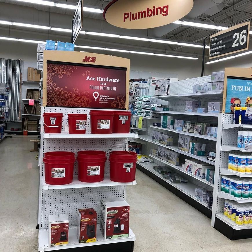 Plumbing aisle in a store with red Ace Hardware bins and product shelves under aisle sign 26