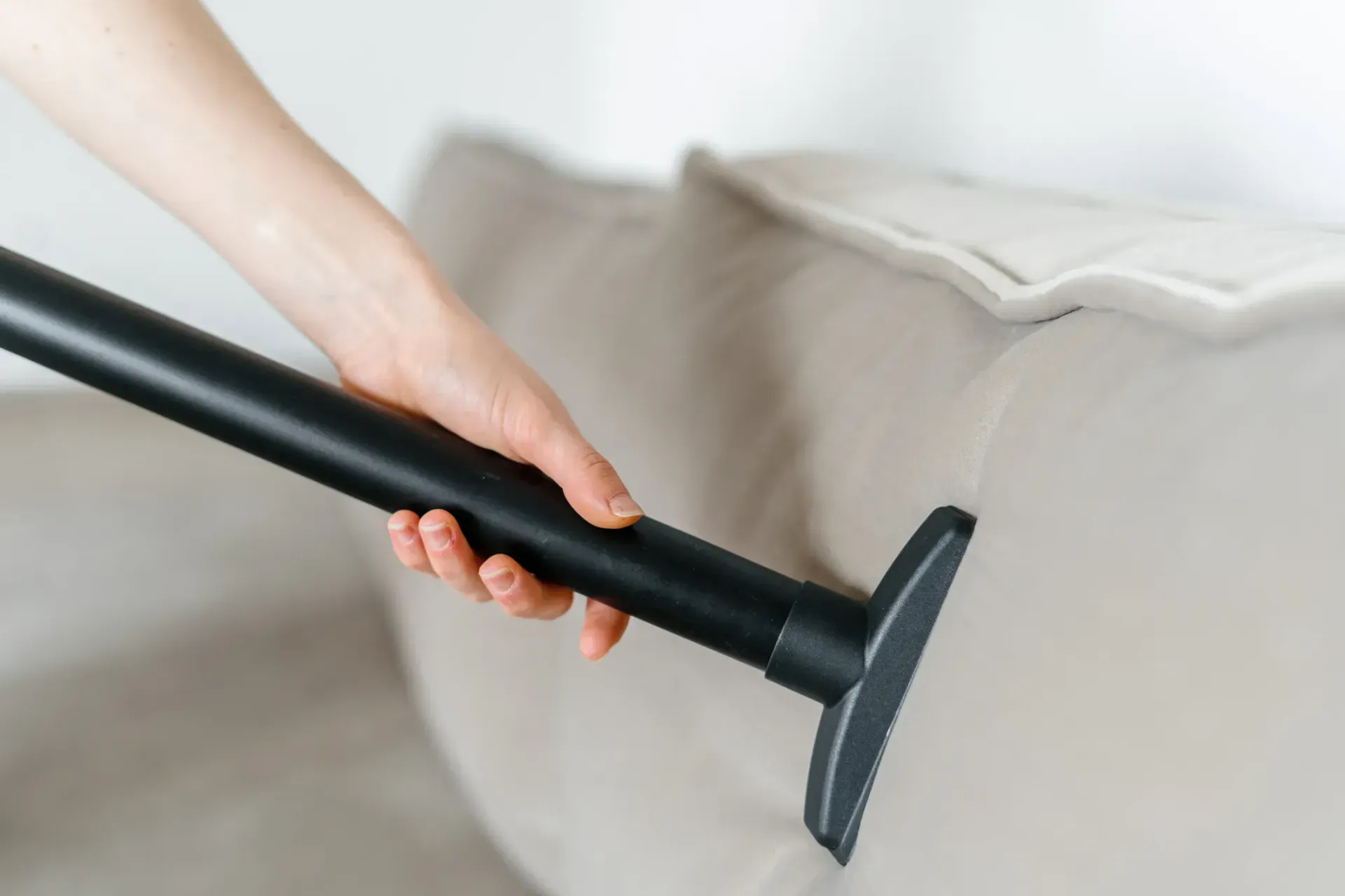 A person is cleaning a couch with a vacuum cleaner.